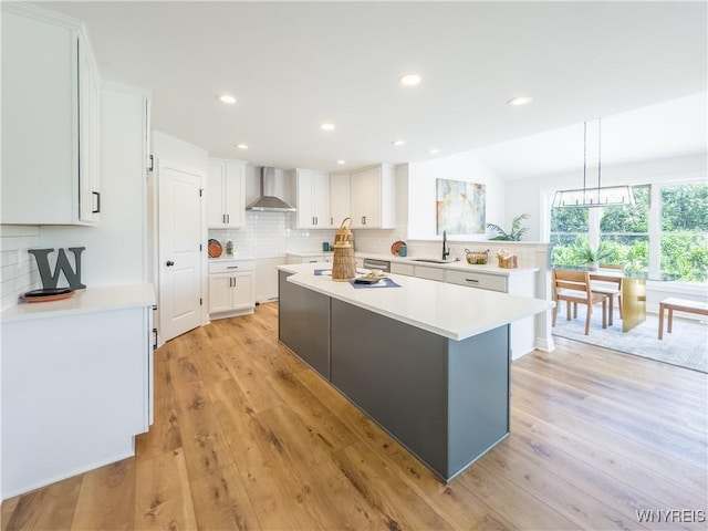 kitchen featuring wall chimney range hood, sink, a center island, and white cabinets