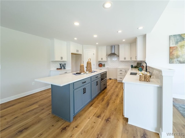 kitchen featuring sink, wall chimney range hood, and white cabinets