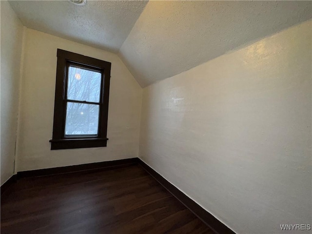 additional living space with dark hardwood / wood-style floors, vaulted ceiling, and a textured ceiling