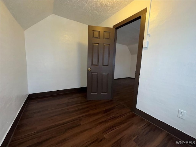 spare room with dark hardwood / wood-style flooring, vaulted ceiling, and a textured ceiling