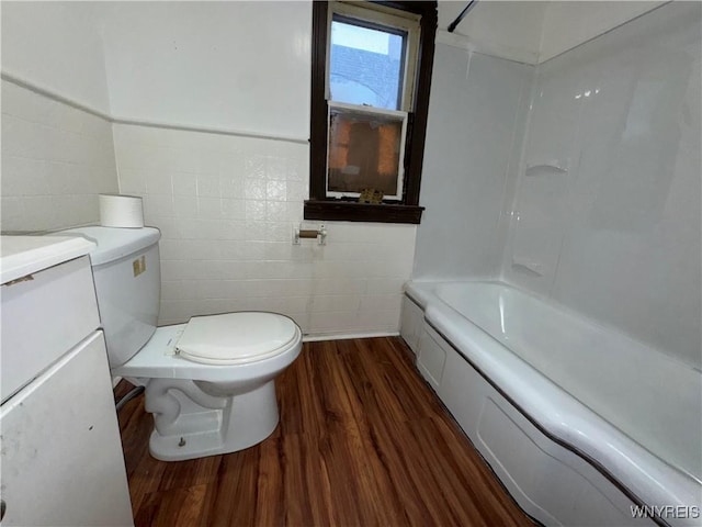 bathroom featuring toilet, wood-type flooring, tile walls, vanity, and a bath