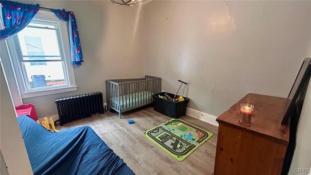 bedroom with radiator, multiple windows, baseboards, and wood finished floors