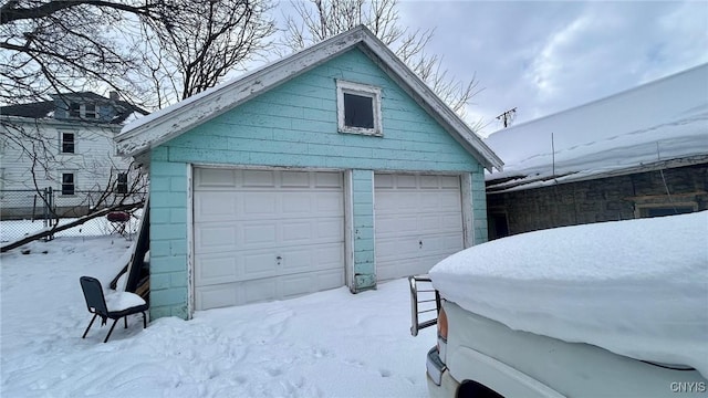 snow covered garage featuring a garage and fence