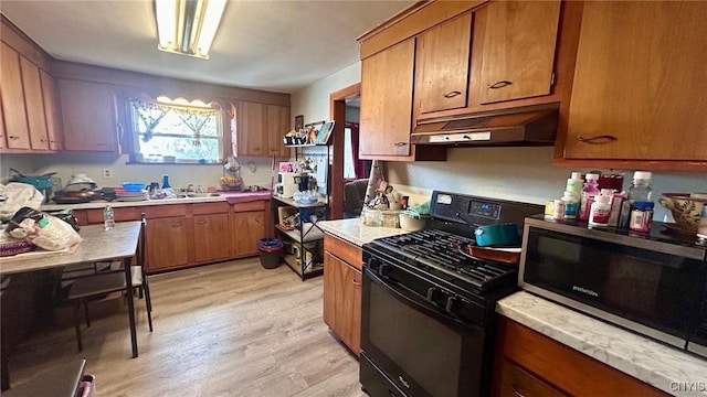 kitchen with under cabinet range hood, light countertops, brown cabinetry, stainless steel microwave, and gas stove