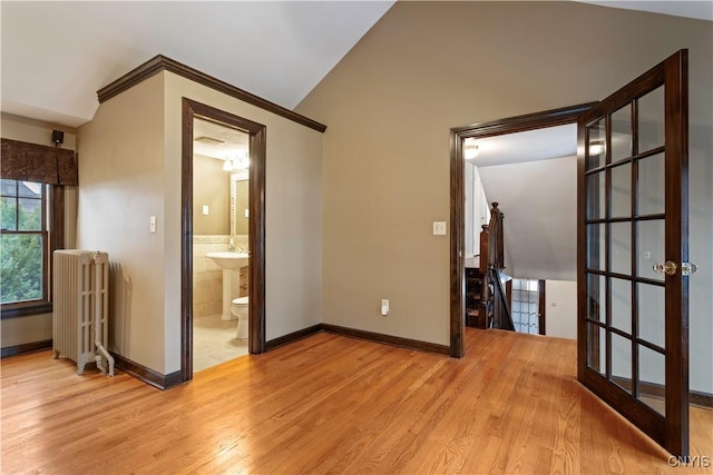 spare room featuring lofted ceiling, radiator heating unit, and light hardwood / wood-style flooring