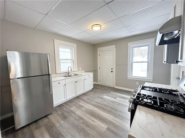 kitchen with sink, stainless steel refrigerator, range hood, range with gas stovetop, and white cabinets