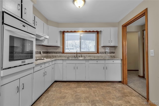 kitchen with tasteful backsplash, white oven, sink, and white cabinets