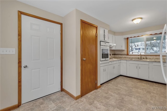 kitchen with white oven, sink, white cabinets, and backsplash