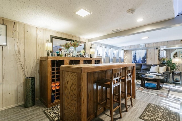 bar with a textured ceiling, light wood-type flooring, and wood walls