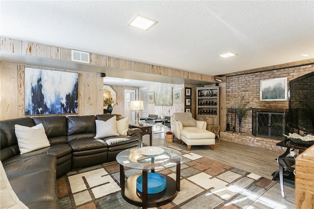 living room with a textured ceiling, light wood-type flooring, wooden walls, brick wall, and a fireplace