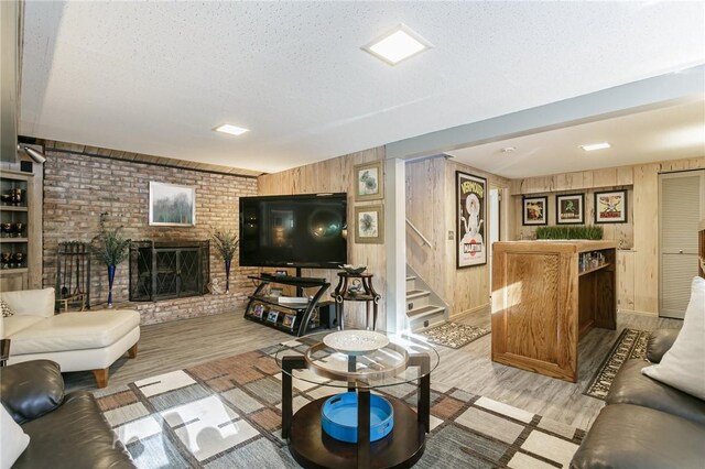 living room with wooden walls, a textured ceiling, a brick fireplace, and light wood-type flooring