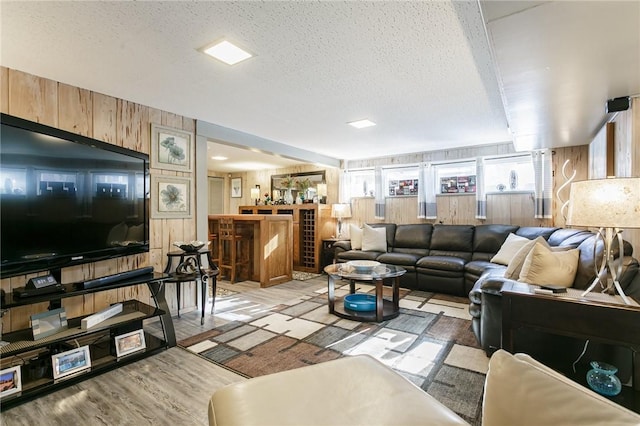 living room with a textured ceiling, light hardwood / wood-style flooring, and wood walls