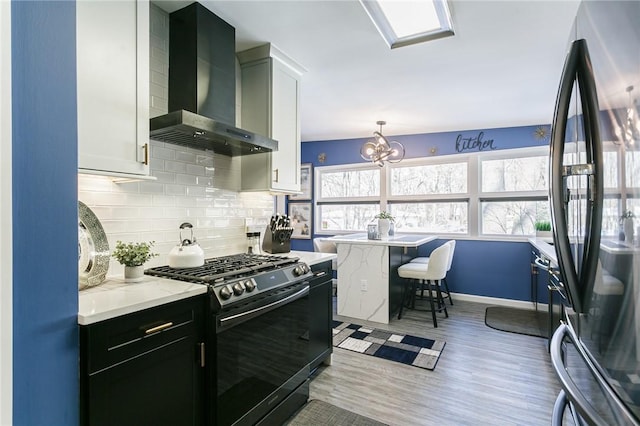 kitchen with wall chimney range hood, white cabinets, black fridge, decorative light fixtures, and stainless steel range with gas cooktop