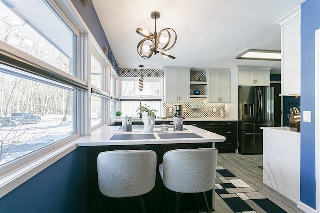 kitchen featuring a kitchen bar, black refrigerator with ice dispenser, white cabinets, pendant lighting, and backsplash