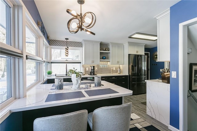 kitchen with pendant lighting, a kitchen breakfast bar, tasteful backsplash, white cabinets, and black refrigerator with ice dispenser