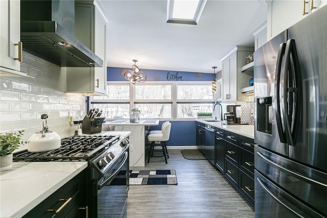 kitchen featuring hanging light fixtures, wall chimney range hood, white cabinets, and black appliances