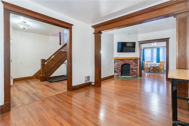 unfurnished living room featuring ornate columns, a brick fireplace, and hardwood / wood-style floors