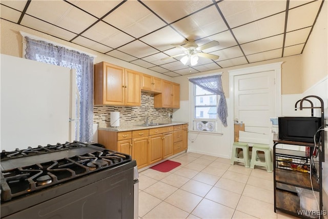 kitchen featuring sink, light tile patterned floors, range with gas stovetop, ceiling fan, and backsplash