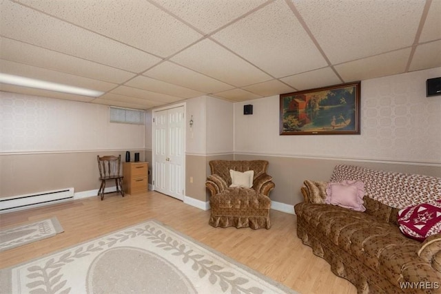 living area with a paneled ceiling, wood-type flooring, and a baseboard heating unit