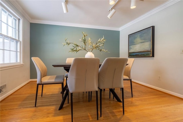 dining room with track lighting, ornamental molding, and light hardwood / wood-style flooring