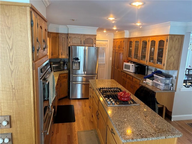 kitchen with light hardwood / wood-style flooring, ornamental molding, a center island, and appliances with stainless steel finishes