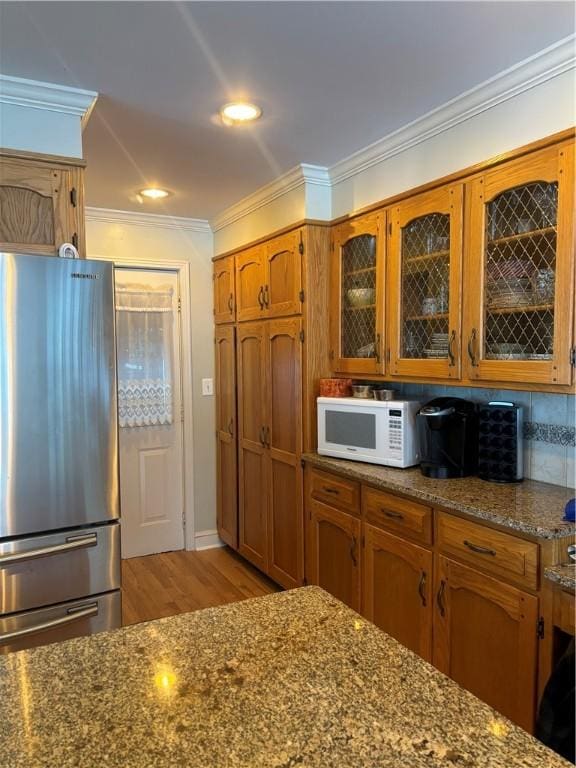 kitchen with stone countertops, stainless steel fridge, decorative backsplash, light hardwood / wood-style floors, and crown molding