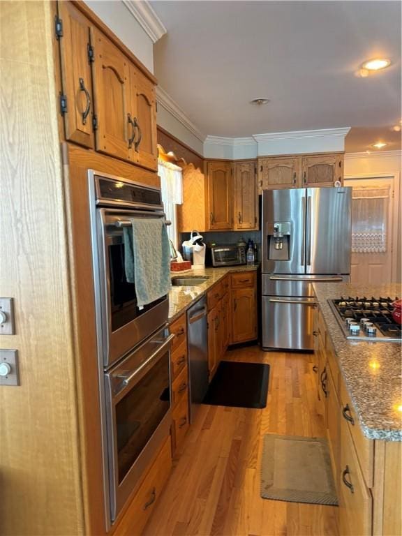 kitchen featuring light stone countertops, crown molding, stainless steel appliances, and light wood-type flooring