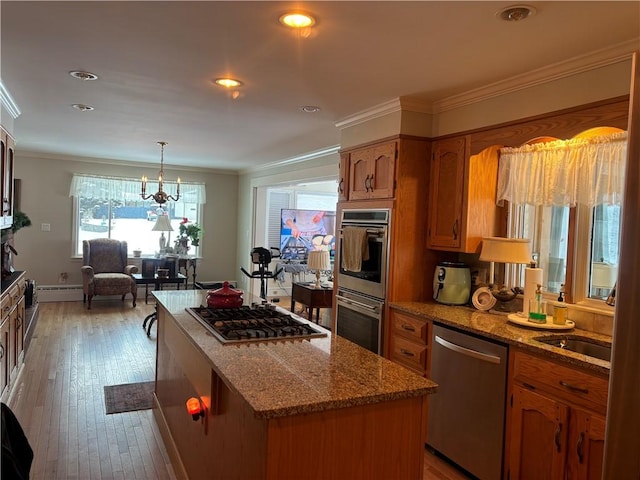 kitchen with hanging light fixtures, ornamental molding, a center island, stainless steel appliances, and light wood-type flooring