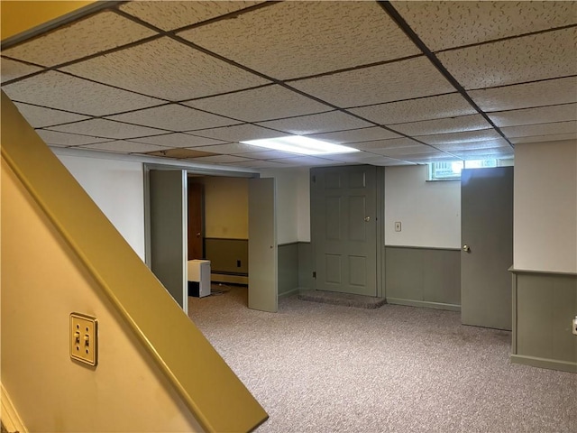 basement with a paneled ceiling, carpet flooring, and a baseboard heating unit