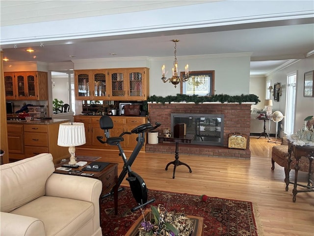 living room featuring ornamental molding, a brick fireplace, a chandelier, and light wood-type flooring