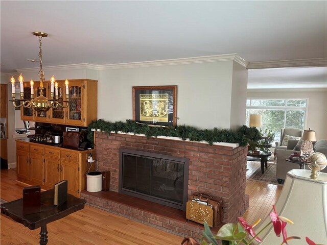 living room with a brick fireplace, crown molding, light hardwood / wood-style flooring, and a notable chandelier