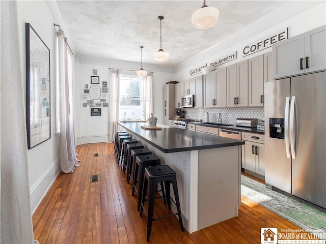 kitchen featuring pendant lighting, a breakfast bar area, stainless steel appliances, a kitchen island, and dark hardwood / wood-style flooring