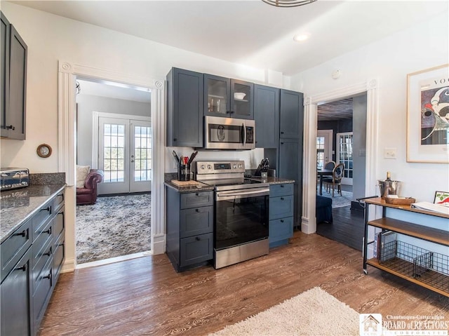 kitchen featuring dark wood-type flooring, gray cabinets, appliances with stainless steel finishes, dark stone countertops, and french doors