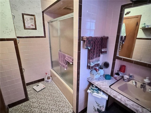 bathroom with sink, tile walls, and shower / bath combination with glass door