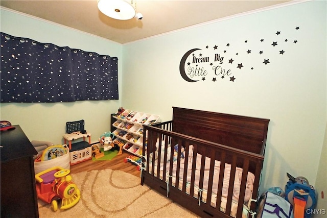 bedroom with crown molding, a nursery area, and hardwood / wood-style flooring