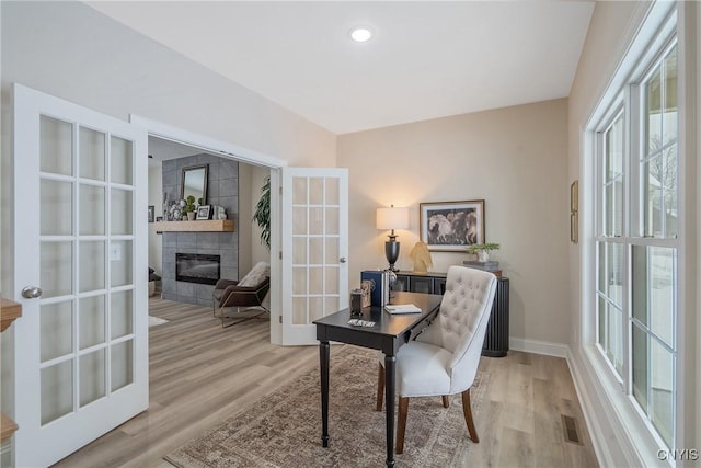 office with light hardwood / wood-style floors, french doors, and a tile fireplace