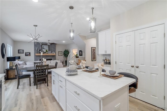 kitchen featuring white cabinetry, hanging light fixtures, a center island, light stone counters, and light hardwood / wood-style floors