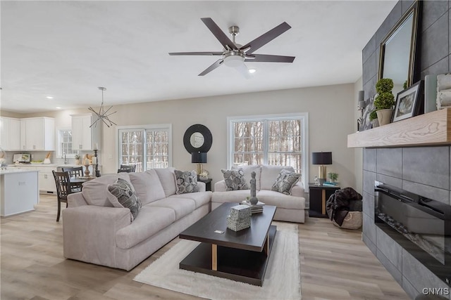 living room with ceiling fan with notable chandelier, a wealth of natural light, and light hardwood / wood-style floors