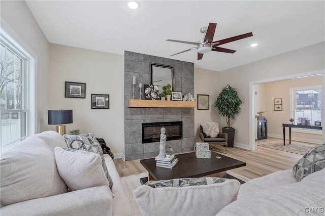 living room with ceiling fan, a tile fireplace, and light hardwood / wood-style flooring