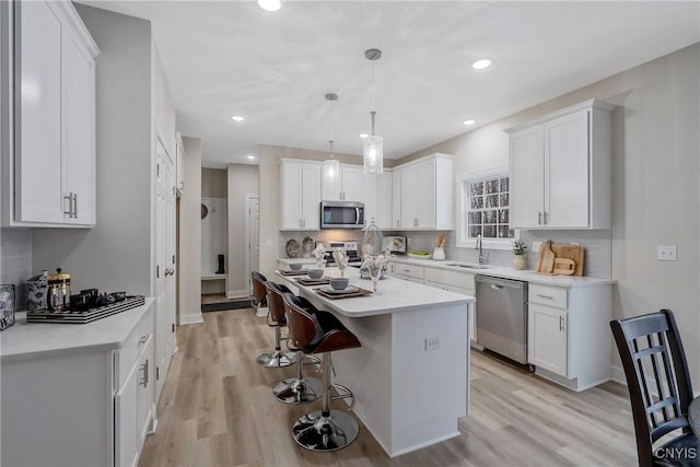 kitchen with a kitchen island, appliances with stainless steel finishes, pendant lighting, white cabinetry, and sink