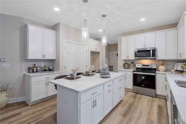 kitchen with hanging light fixtures, stainless steel appliances, white cabinets, and light wood-type flooring