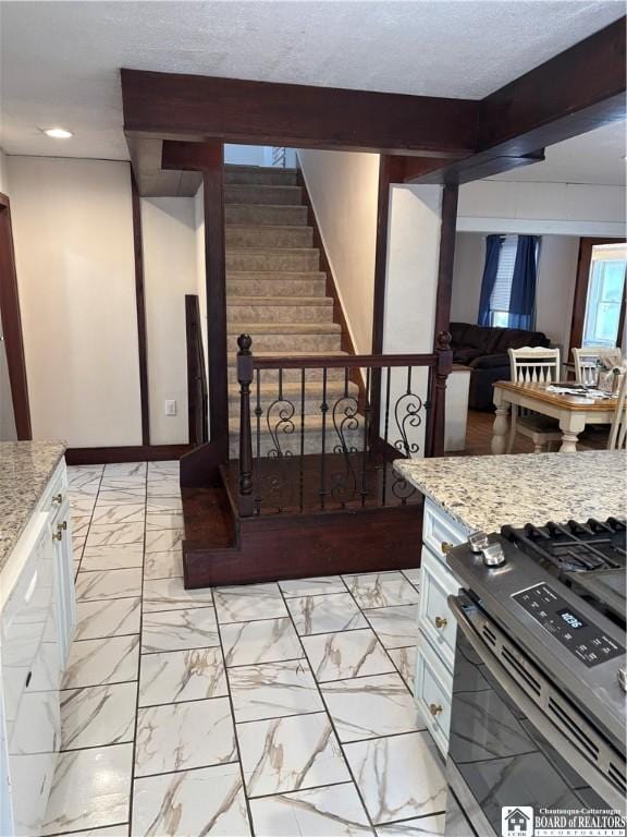 kitchen with light stone counters, stainless steel range with gas stovetop, beam ceiling, and white cabinets