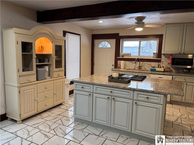 kitchen featuring sink, a kitchen island, ceiling fan, beam ceiling, and light stone countertops