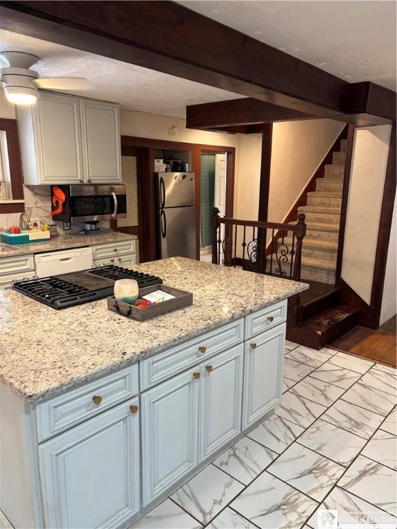 kitchen with light stone counters, stainless steel appliances, and beamed ceiling