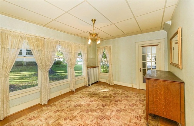 unfurnished sunroom with radiator heating unit and a drop ceiling