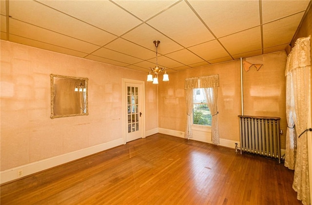 empty room with a paneled ceiling, radiator heating unit, hardwood / wood-style floors, and a notable chandelier