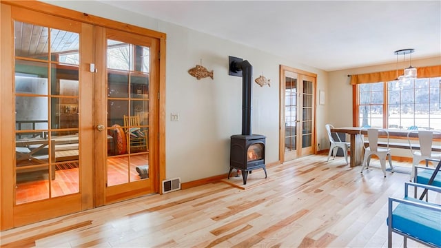 dining space featuring french doors, light hardwood / wood-style flooring, and a wood stove