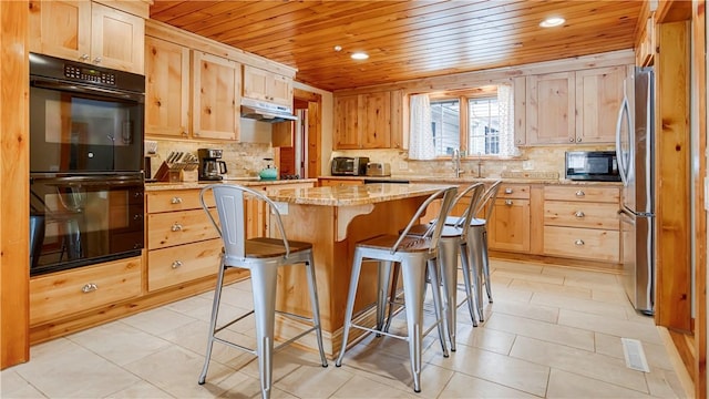 kitchen featuring sink, a breakfast bar area, a center island, light stone countertops, and black appliances