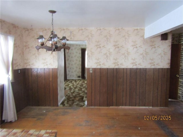 unfurnished dining area with wallpapered walls, wooden walls, a chandelier, and wainscoting