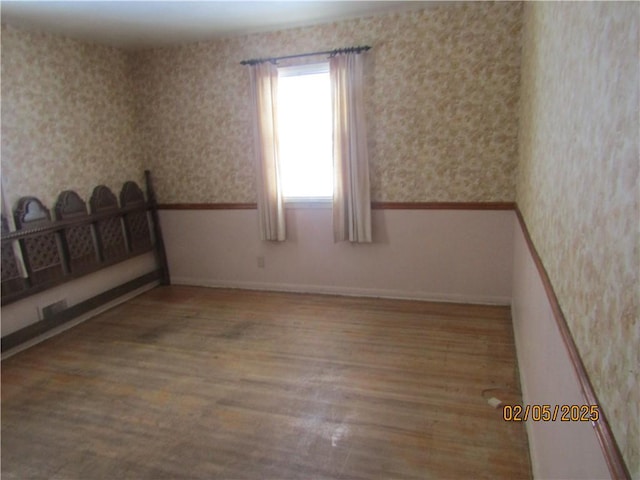 unfurnished room featuring wainscoting, wallpapered walls, and wood finished floors